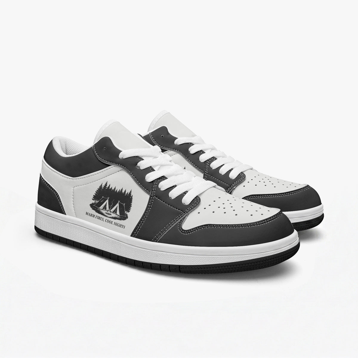 Angled three-quarter view of low-top sneakers in charcoal black and white leather, featuring a campsite in the woods illustration with "WARM FIRES, COOL NIGHTS", white laces, and a white inner lining.