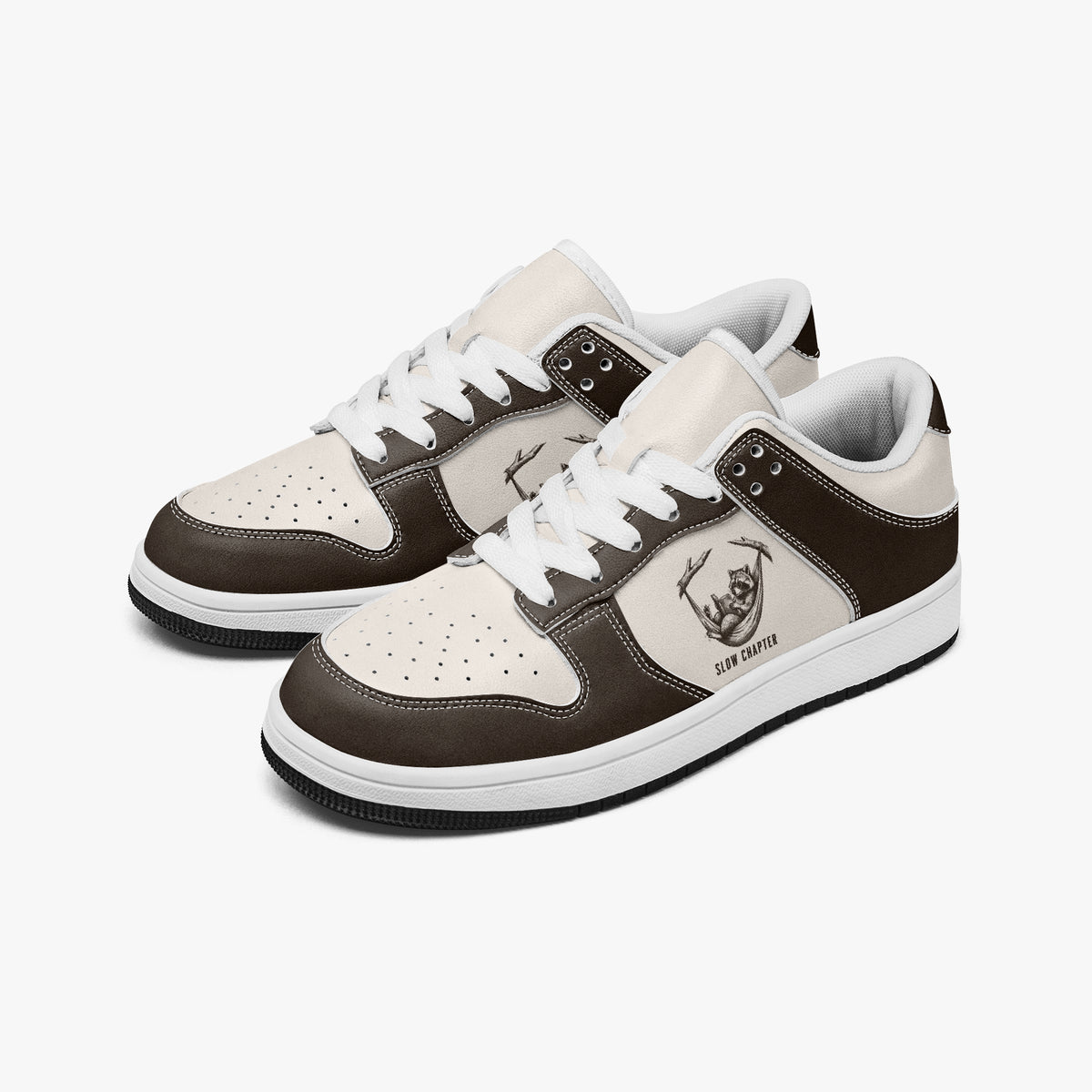 Angled three-quarter view of low-top sneakers in dark espresso brown and cream leather, featuring a raccoon in a hammock illustration with "SLOW CHAPTER", white laces, and a white inner lining.
