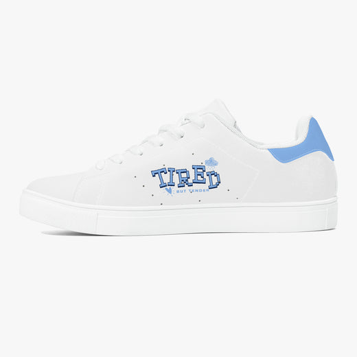A white low-top sneaker with a light blue heel tab and a blue 'TIRED' graphic on the side, set against a plain light gray background.