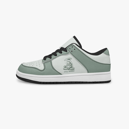 Side profile view of the left sneaker highlighting the sage green leather panels, frog graphic, black interior lining, and flat rubber sole facing right.