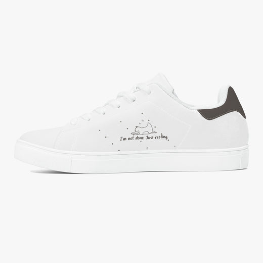 A white low-top sneaker with a black heel tab, featuring a small sleeping cat illustration and the text 'I'm not done. Just resting.