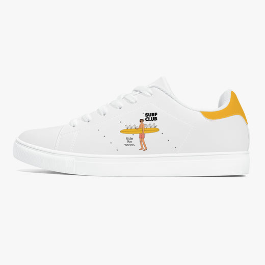 A white low-top sneaker with a yellow heel tab and a cartoon graphic of a surfer carrying drinks on the side. The graphic includes the text 'SURF CLUB' and 'BIG BOY MOVIES'.