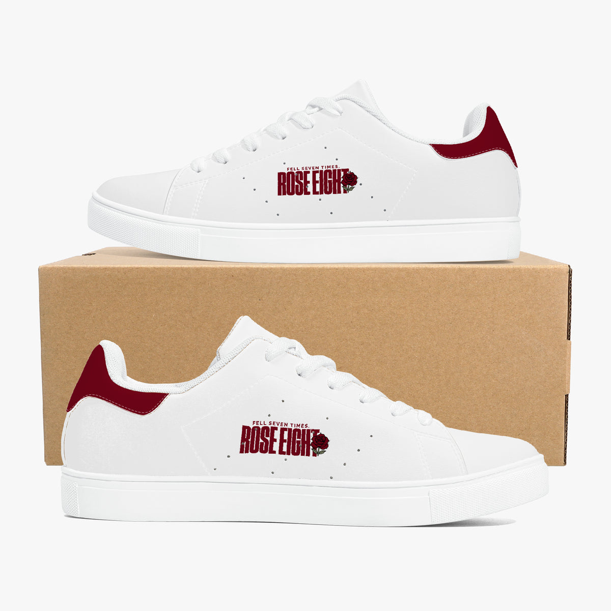 A pair of white low-top sneakers with dark red heel tabs and a dark red 'The Walking Dead Rose Eight' graphic on the side, displayed on a brown cardboard shoebox against a light gray background.