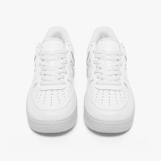 Front view of a pair of minimalist all-white low-top leather sneakers with white laces and perforated toe caps on a clean white background.
