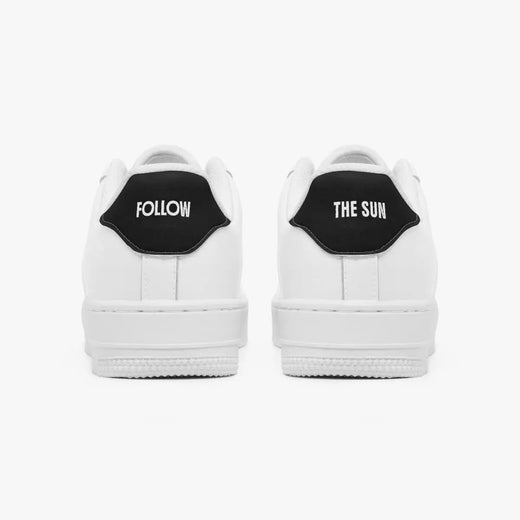 A pair of white low-top sneakers shown from the back, featuring a black heel tab with white text reading 'FOLLOW' on the left shoe and 'THE SUN' on the right shoe, set against a plain light gray background.