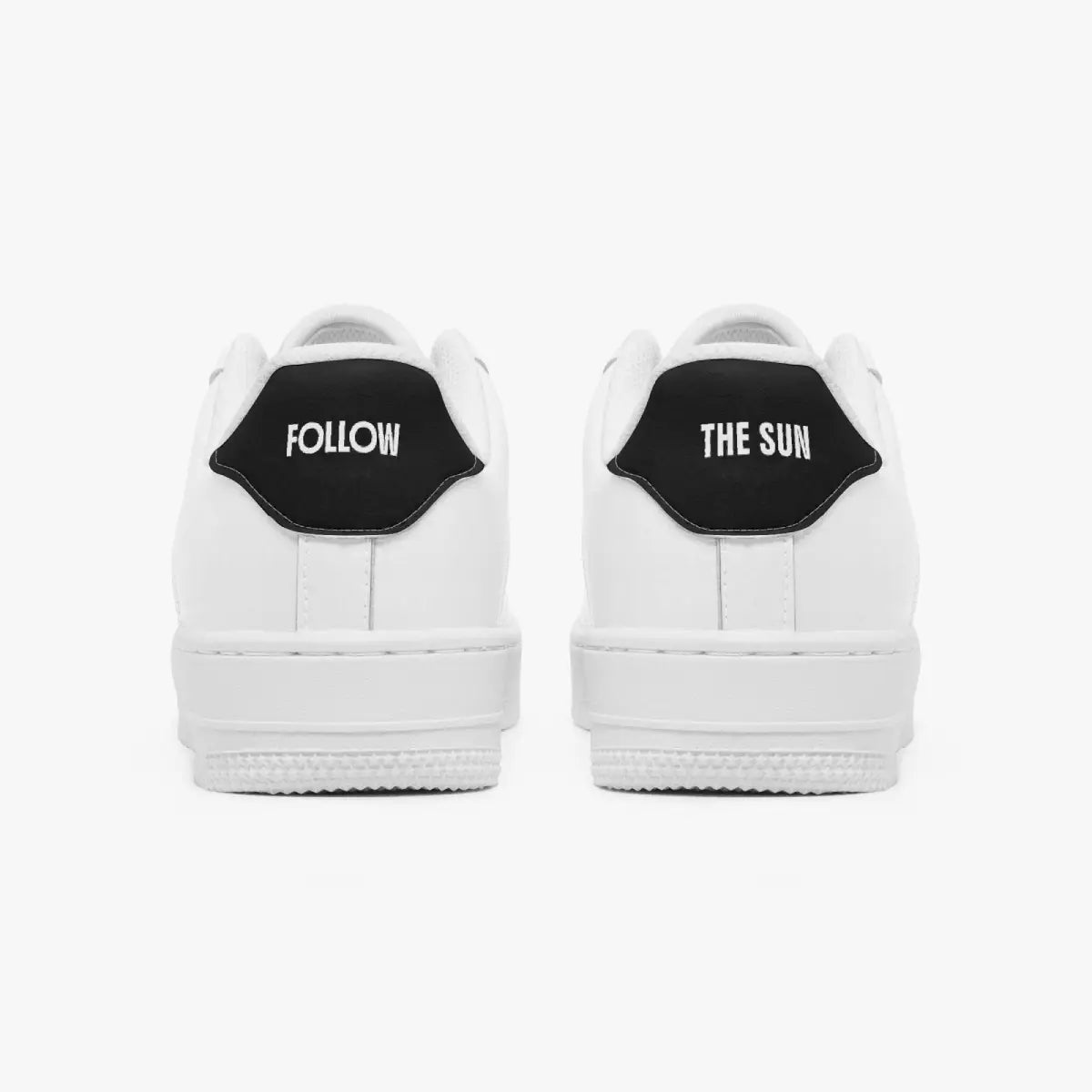 A pair of white low-top sneakers shown from the back, featuring a black heel tab with white text reading 'FOLLOW' on the left shoe and 'THE SUN' on the right shoe, set against a plain light gray background.
