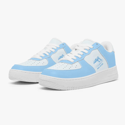 Angled three-quarter view of sky blue and white low-top sneakers, featuring a leaping dolphin graphic with "CHASE THE WAVE", white laces, and thick white rubber soles.