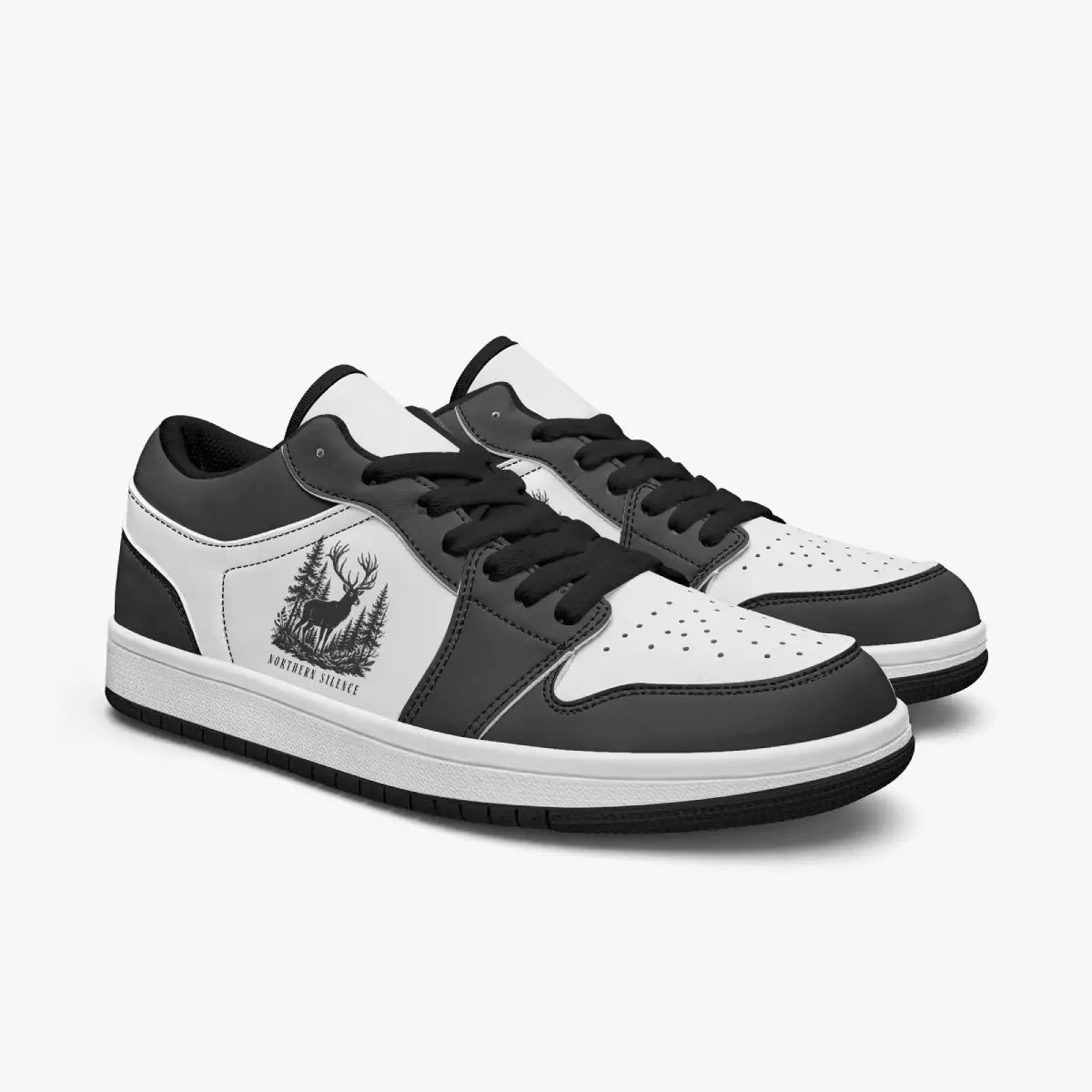 Angled three-quarter view of low-top sneakers in charcoal black and white leather, displaying the "NORTHERN SILENCE" stag emblem, black laces, and a black interior lining.