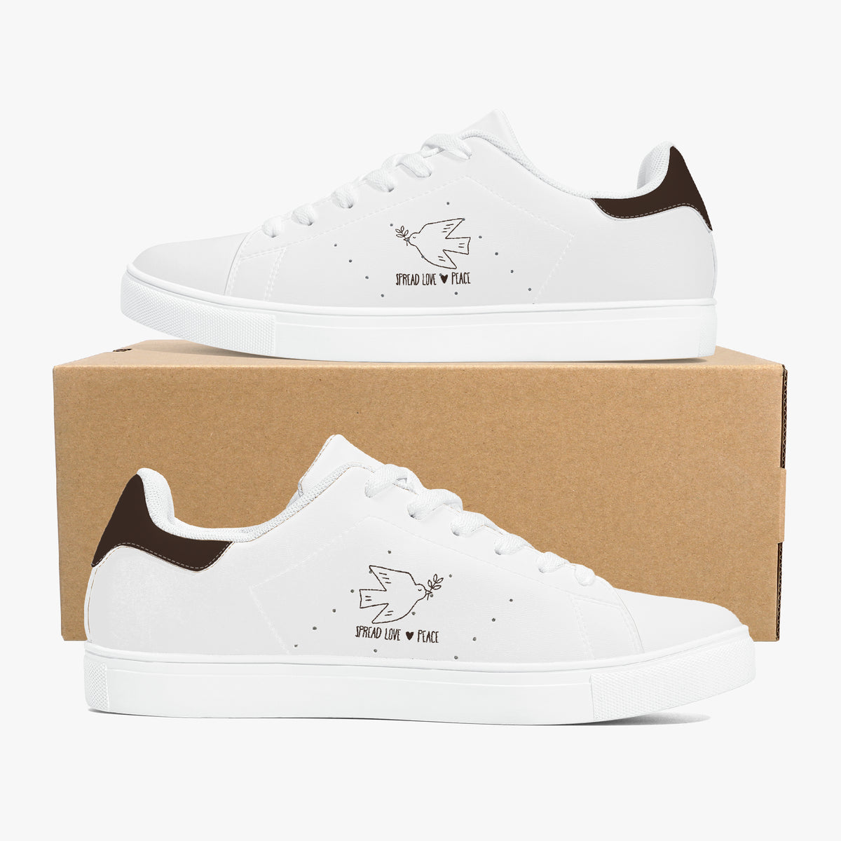 A pair of white low-top sneakers with dark brown heel accents and a small black dove graphic with the words 'SEND LOVE * PEACE' on the side, displayed on and in front of a brown cardboard box against a light gray background.
