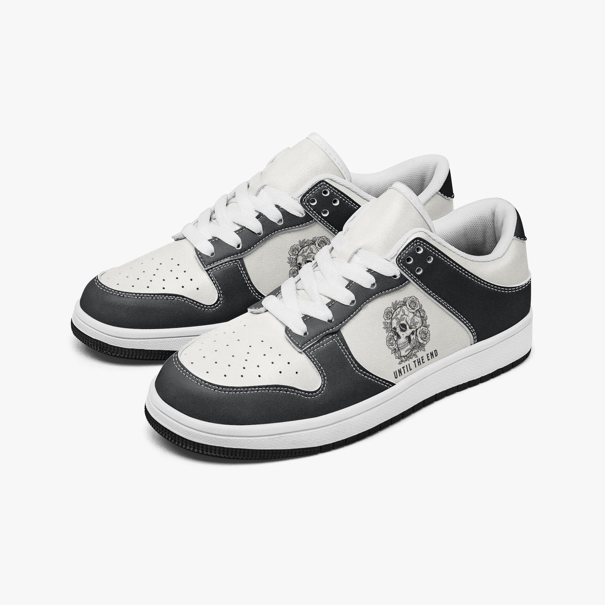 Angled three-quarter view of low-top sneakers in charcoal black and white leather, featuring a floral skull illustration with "UNTIL THE END", white laces, and a white inner lining.