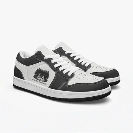 Angled three-quarter view of low-top sneakers in charcoal black and white leather, featuring a campsite in the woods illustration with "WARM FIRES, COOL NIGHTS", white laces, and a white inner lining.