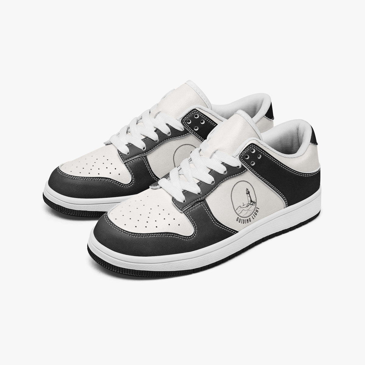 Angled three-quarter view of low-top sneakers in charcoal black and white leather, featuring a lighthouse by the sea graphic with "GUIDING LIGHT", white laces, and a white inner lining.