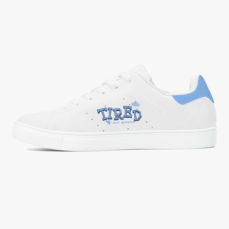 A white low-top sneaker with a light blue heel tab and a blue 'TIRED' graphic on the side, set against a plain light gray background.