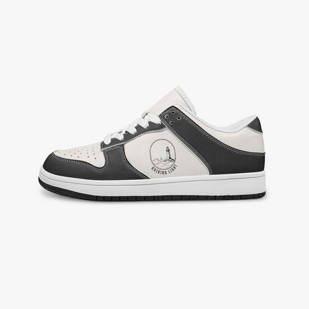 Side profile view of the left sneaker in black and white leather, highlighting the "GUIDING LIGHT" lighthouse design, white laces, white interior lining, and flat rubber sole facing right.