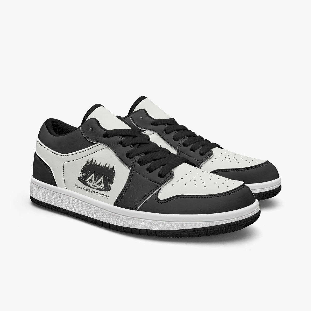 Angled three-quarter view of low-top sneakers in charcoal black and white leather, displaying the "WARM FIRES, COOL NIGHTS" camp graphic, black laces, and a black interior lining.