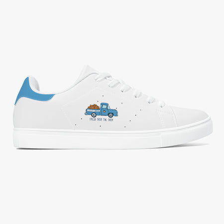 A white low-top sneaker with a light blue heel tab, white laces, and a small graphic of a blue pickup truck carrying orange pumpkins on the side. The text 'THIS GOES TO GIR' is printed below the truck.