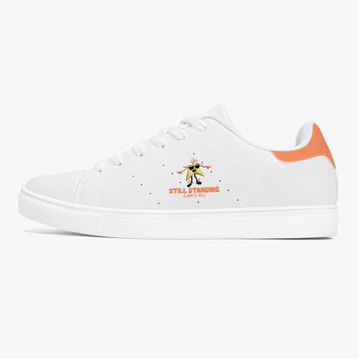 A white low-top sneaker with a white rubber sole, featuring a small graphic of a dancing figure and the text 'STILL STANDING ALWAYS WILL' on the side, with an orange heel accent.