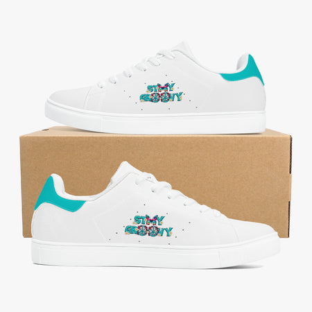 A pair of white low-top sneakers with turquoise heel accents and colorful 'STAY AND BREATHE' text on the side, displayed on a brown cardboard box against a light gray background.