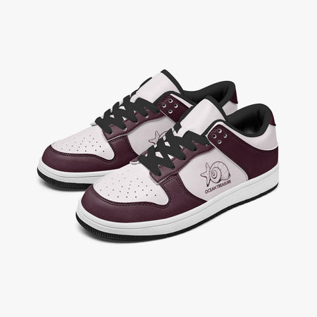 Angled three-quarter view of low-top sneakers in burgundy and pale pink leather, featuring a seashell and starfish illustration with "OCEAN TREASURE", black laces, and a black inner lining.