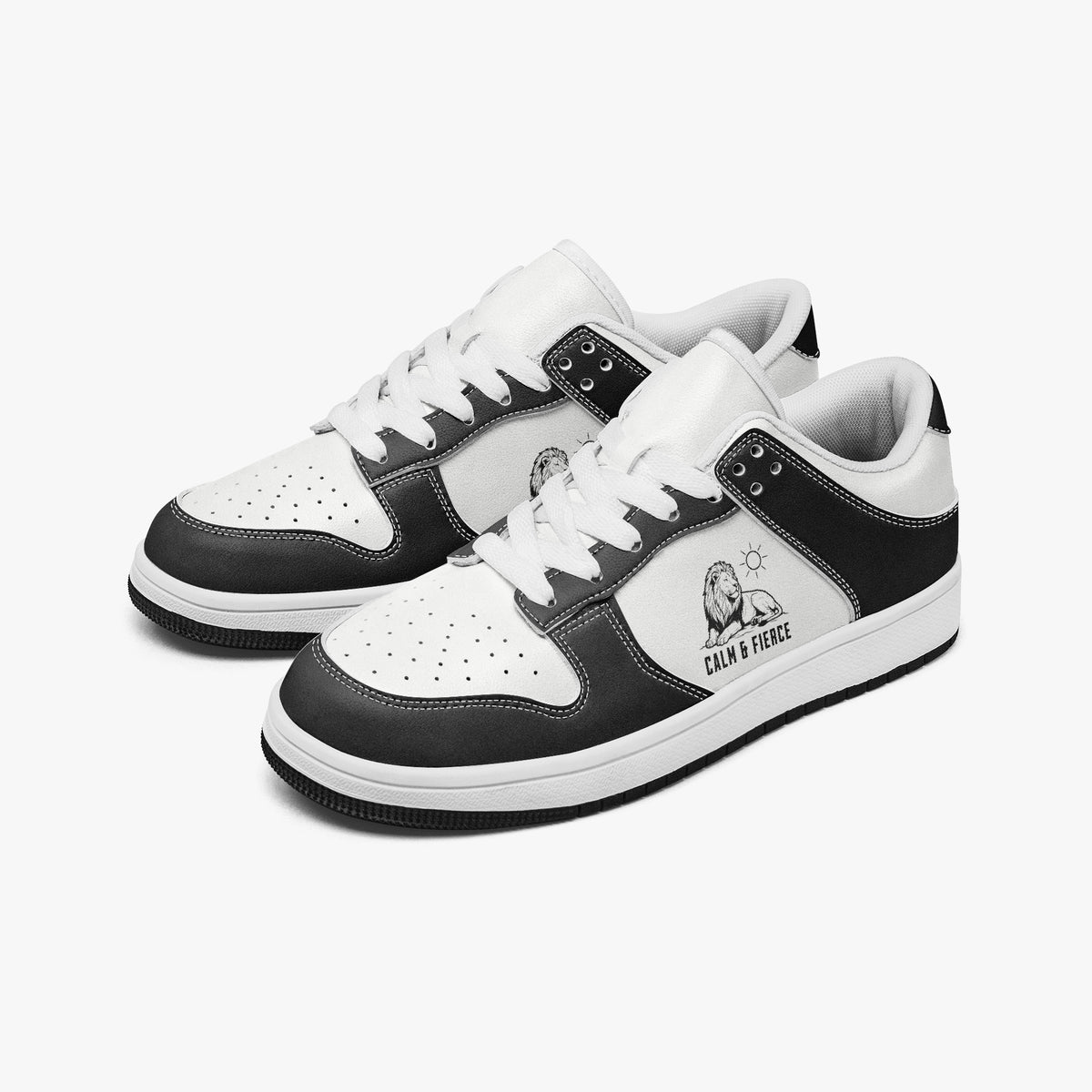 Angled three-quarter view of low-top sneakers in charcoal black and white leather, featuring a resting lion graphic with "CALM & FIERCE", white laces, and a white inner lining.