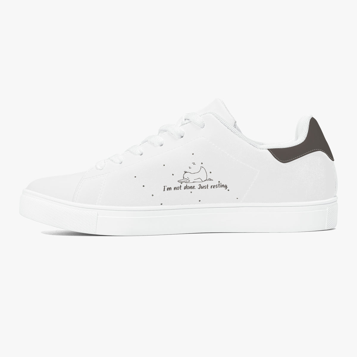 A white low-top sneaker with a black heel tab, featuring a small sleeping cat illustration and the text 'I'm not done. Just resting.