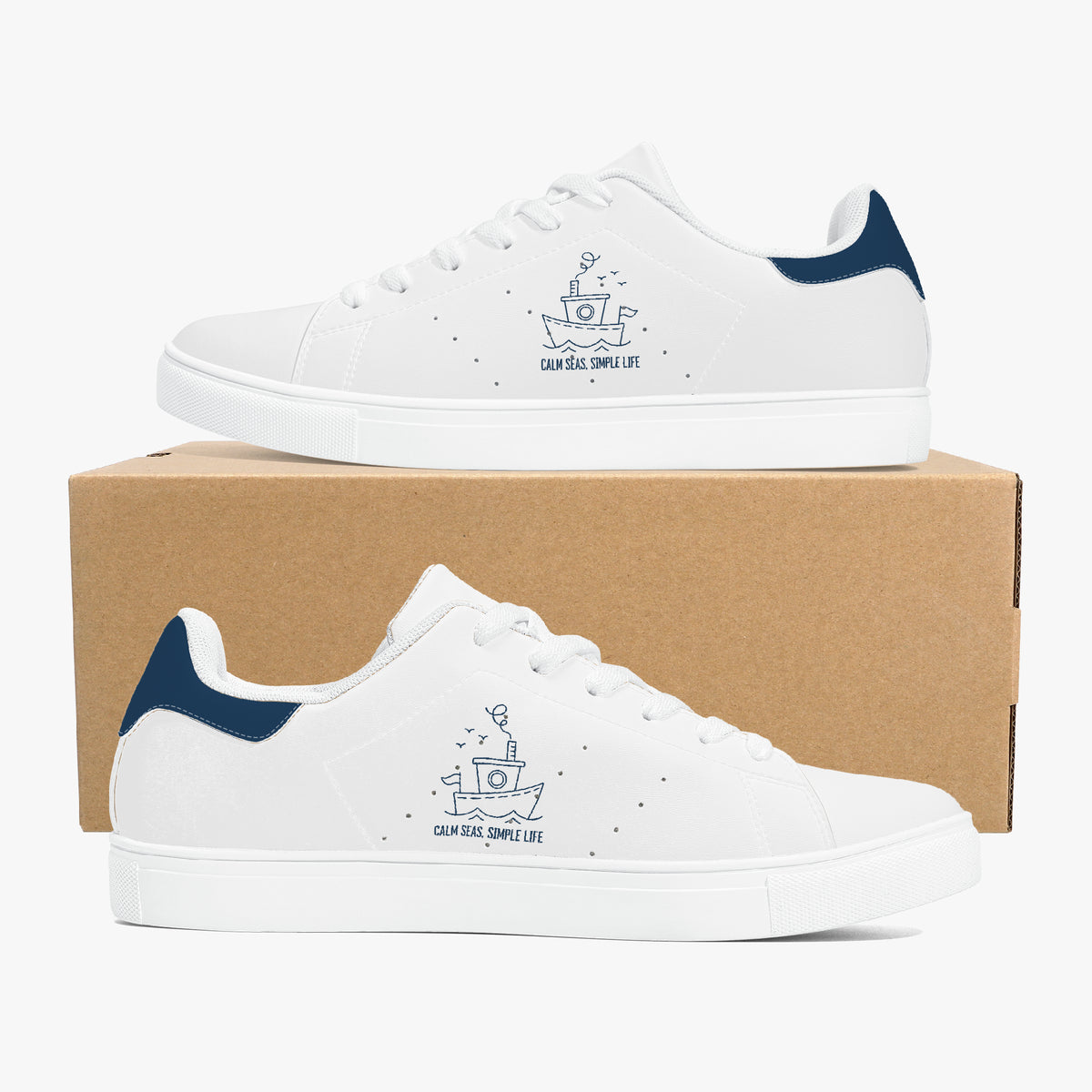 A pair of white low-top sneakers with navy blue heel accents and a navy blue boat graphic with the text 'Cruiser, Cruise Life' on the side, displayed on and in front of a brown cardboard shoebox against a light gray background.