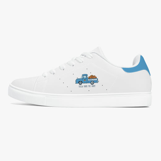 A white low-top sneaker with a blue heel accent and a small graphic of a blue pickup truck carrying a brown dog on its bed. The side of the shoe features the text 'TEACH DOG TO PACK' in black, with tiny black star-like specks scattered around the graphic.