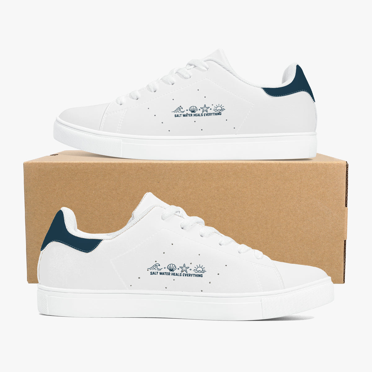 A pair of white low-top sneakers with dark teal accents on the heel tab and navy blue printed graphics on the side, displayed on top of and in front of a brown cardboard box against a light gray background.