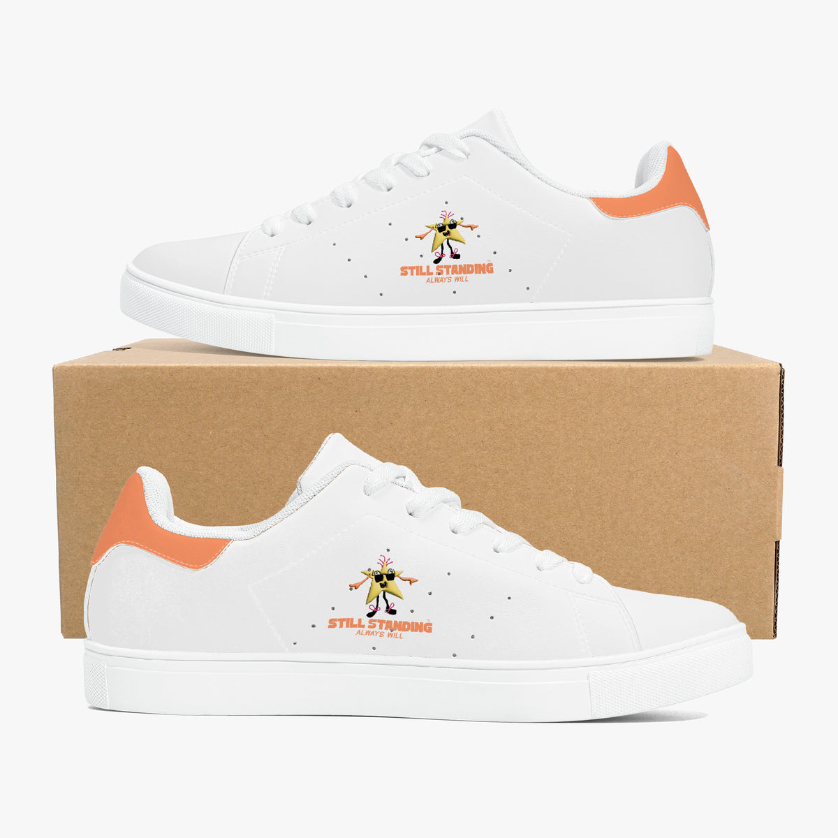 A pair of white low-top sneakers with orange heel accents and a small graphic on the side, displayed on top of and in front of a brown cardboard box against a light gray background.