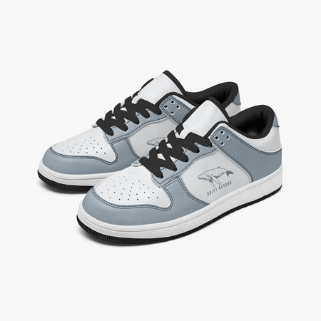 Angled three-quarter view of low-top sneakers in slate blue-grey and white leather, featuring a whale graphic with "DRIFT BEYOND", black laces, and a black inner lining.
