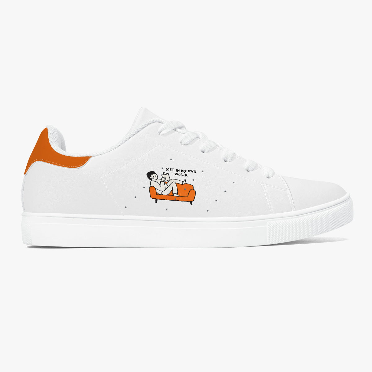 A white low-top sneaker with an orange heel tab and a small cartoon graphic on the side showing a person sitting on an orange couch with the text 'LOST IN MY OWN WORLD'.