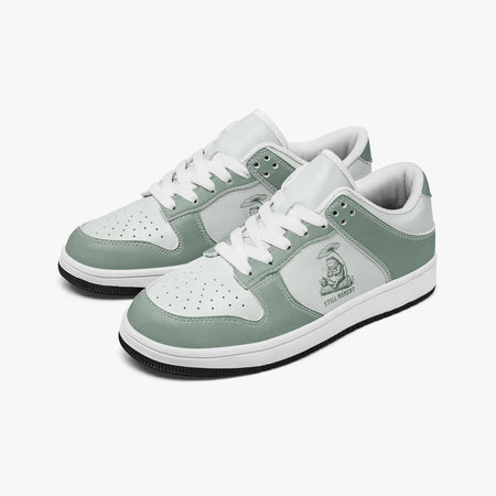 Angled three-quarter view of low-top sneakers in sage green and off-white leather, featuring a frog under a lotus leaf graphic with "STILL MOMENT", white laces, and a white inner lining.