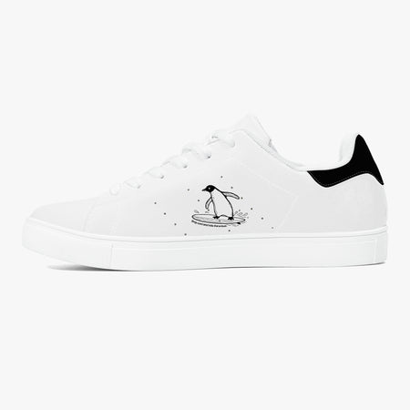 A white low-top sneaker with a black heel tab, featuring a black line-art illustration of a penguin standing on a surfboard on the side, set against a plain white background.