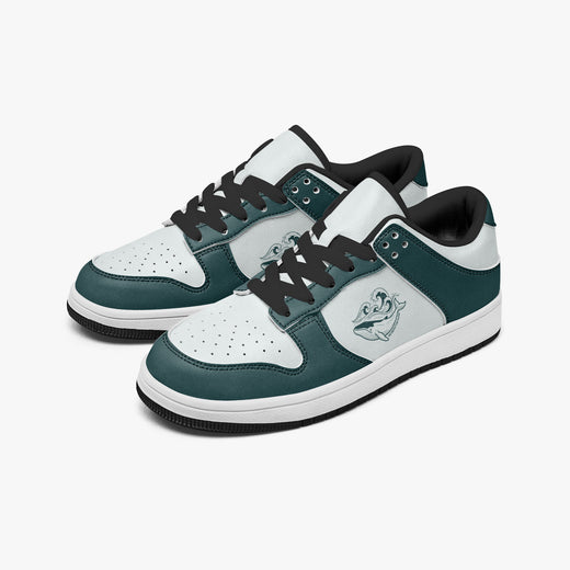 Angled three-quarter view of low-top sneakers in dark teal green and white leather, featuring a whale with ocean waves graphic on the side panel and black laces.