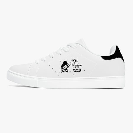 A white low-top sneaker with a black heel tab, white laces, and a black graphic on the side depicting a penguin on a surfboard with the text 'Penguin Surf Waves'.