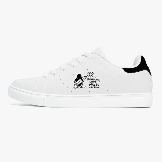 A white low-top sneaker with a black heel tab, white laces, and a black graphic on the side depicting a penguin on a surfboard with the text 'Penguin Surf Waves'.