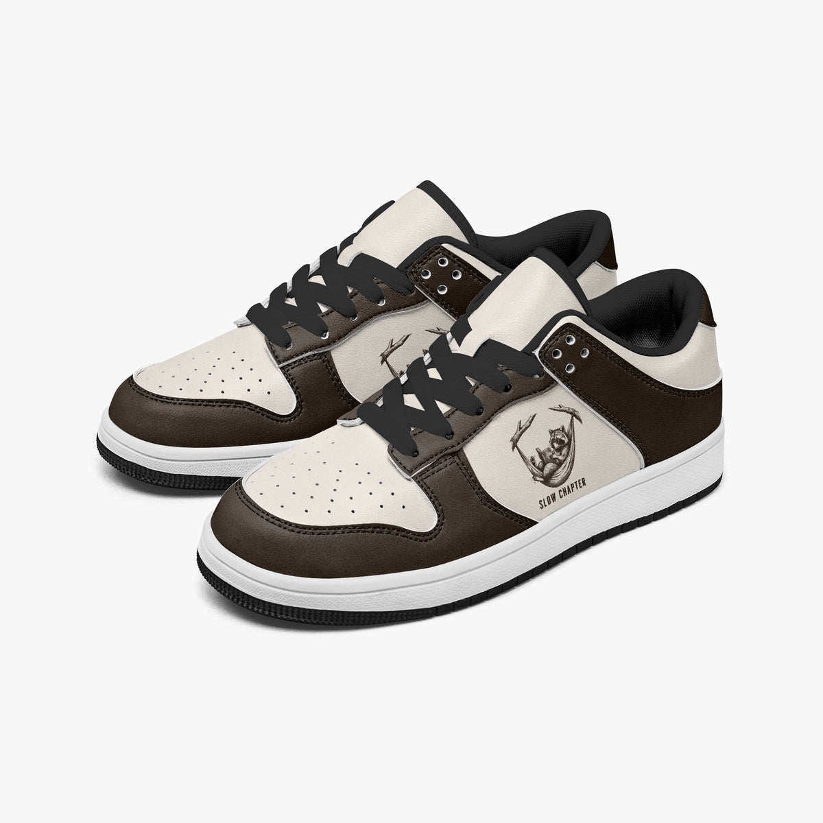 Angled three-quarter view of low-top sneakers in dark espresso brown and cream leather, featuring a raccoon relaxing in a hammock graphic with "SLOW CHAPTER", black laces, and a black inner lining.