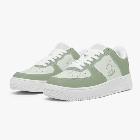 Angled three-quarter view of sage green and light mint low-top sneakers, featuring a frog sitting on a lily pad graphic with "PATIENT MIND", white laces, and thick white rubber soles.