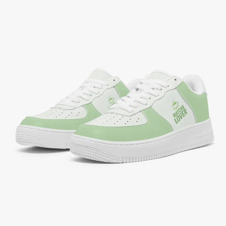 Angled three-quarter view of green and white sneakers featuring a steaming teacup icon and "MATCHA LOVER" graphic printed on the side panel.