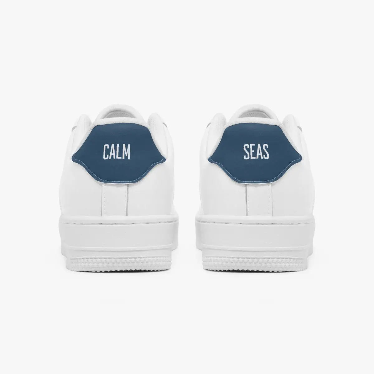 Rear view of white low-top sneakers showing contrasting navy blue heel tabs labeled "CALM" and "SEAS" above solid white rubber soles.