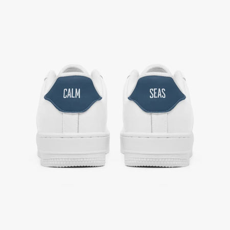 Rear view of white low-top sneakers showing contrasting navy blue heel tabs labeled "CALM" and "SEAS" above solid white rubber soles.
