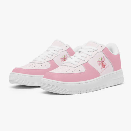 Angled three-quarter view of pink and white sneakers featuring a strawberry with a pink ribbon bow and "Sweet as a berry" graphic printed on the side panel.
