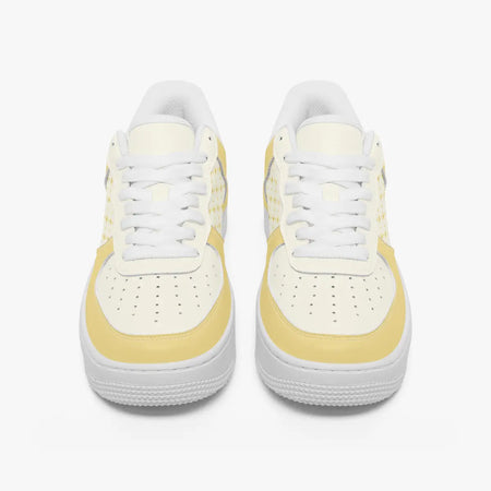 Front view of a pair of pastel yellow and cream low-top leather sneakers with white laces and perforated toe caps on a clean white background.