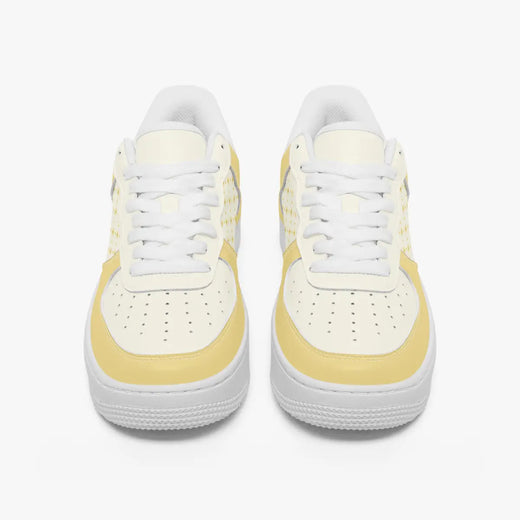 Front view of a pair of pastel yellow and cream low-top leather sneakers with white laces and perforated toe caps on a clean white background.
