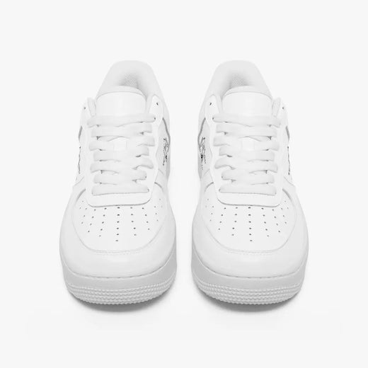 Front view of a pair of minimalist all-white low-top leather sneakers with white laces and perforated toe caps on an isolated white background.