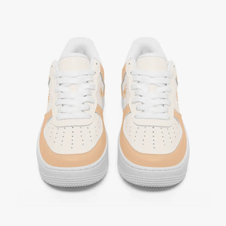 A pair of low-top sneakers shown from the front on a light gray background. The shoes are primarily white with a warm peach-beige accent panel around the midfoot and toe area.