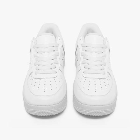 Front view of a pair of minimalist all-white low-top leather sneakers with white laces and perforated toe caps on a clean white background.