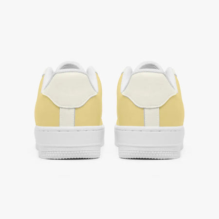 Rear view of a pair of pastel yellow and cream sneakers showing the padded heel counters and flat white rubber soles.