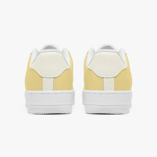 Rear view of a pair of pastel yellow and cream sneakers showing the padded heel counters and flat white rubber soles.
