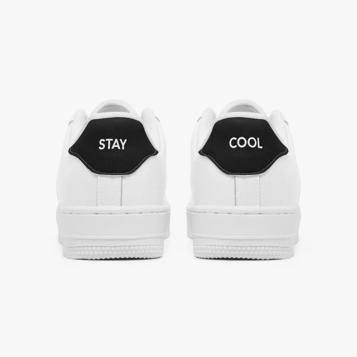 Rear view of white low-top sneakers showing contrasting black heel tabs labeled "STAY" and "COOL" above solid white rubber soles.